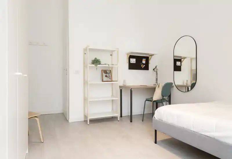 Bright, minimalist bedroom with a comfortable bed, a desk and shelving; clean lines and soft natural light make it ideal for rental listings.