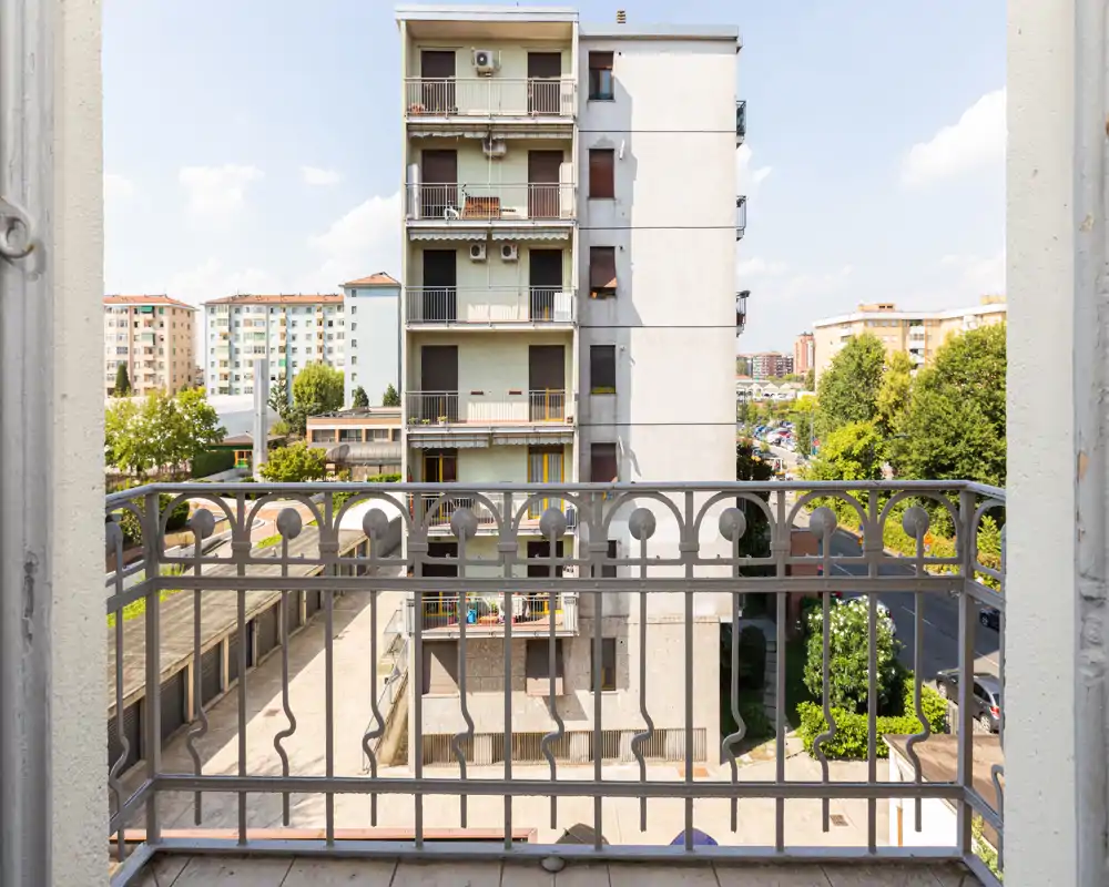 Sunny balcony view with decorative wrought-iron railing overlooking neighboring apartment buildings and tree-lined streets, ideal for a morning coffee.