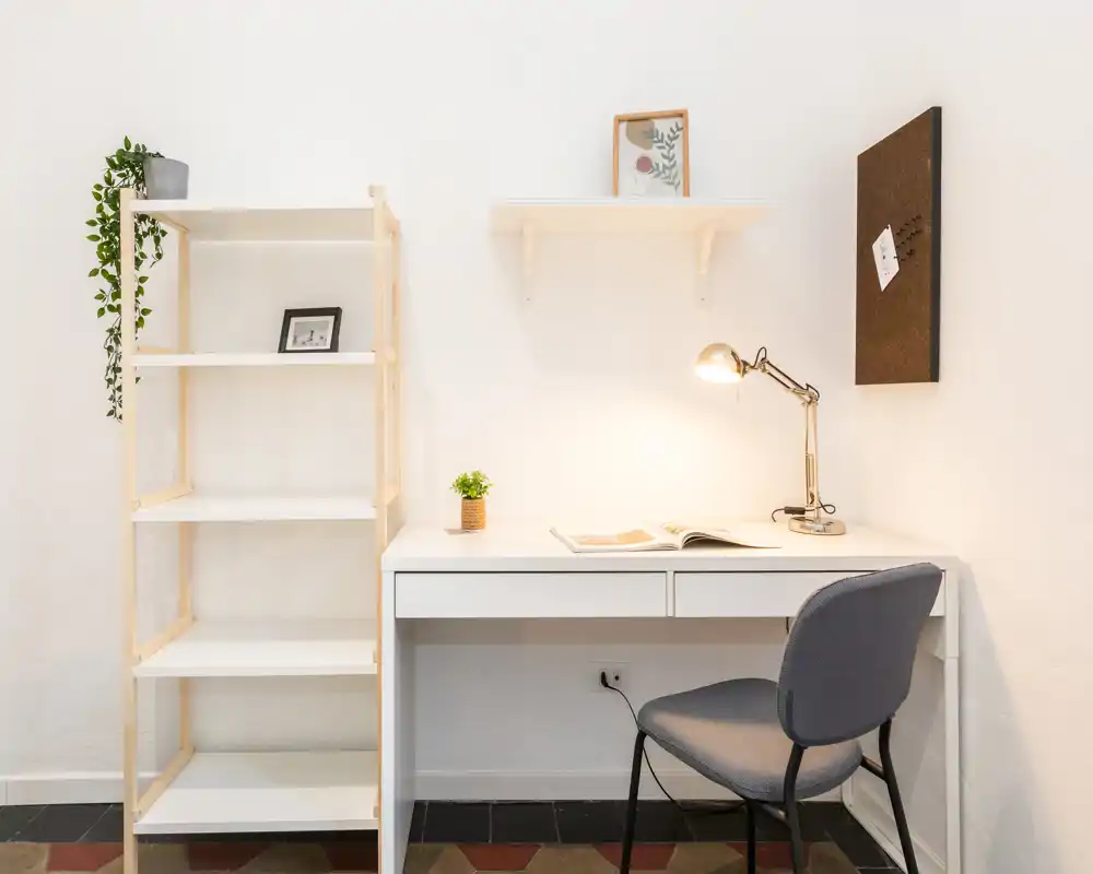 Angolo studio minimalista e luminoso con scrivania bianca, lampada da tavolo, scaffale e sedia comoda — perfetto per lavorare o studiare concentrati.