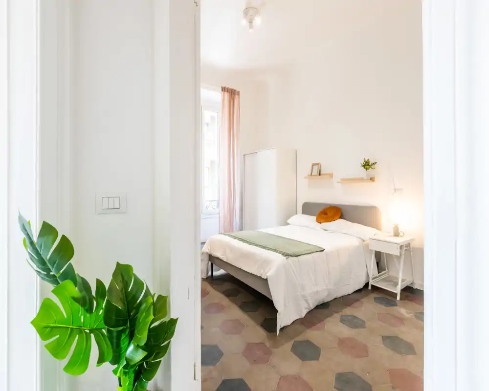 Camera da letto luminosa e ben allestita con letto matrimoniale, comodino e tessili morbidi; la luce naturale dalla finestra crea un'atmosfera accogliente.