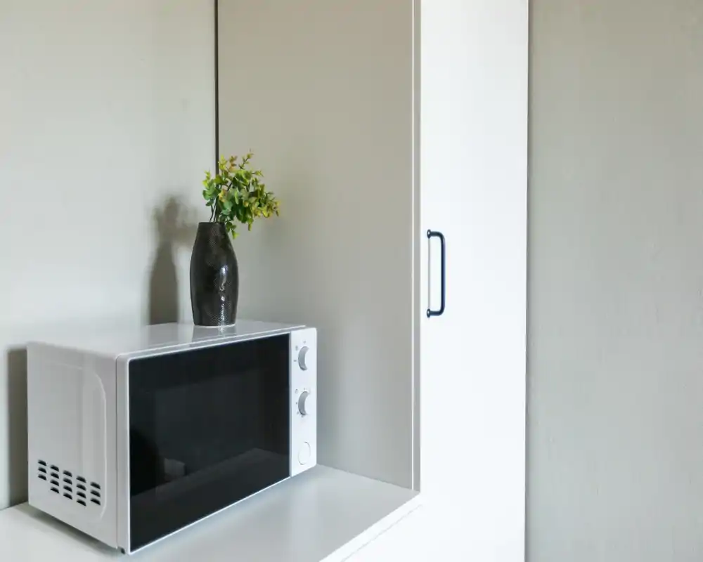 Angolo cucina compatto con un forno a microonde bianco su una mensola pulita e un vaso decorativo, ideale per appartamenti piccoli o monolocali.