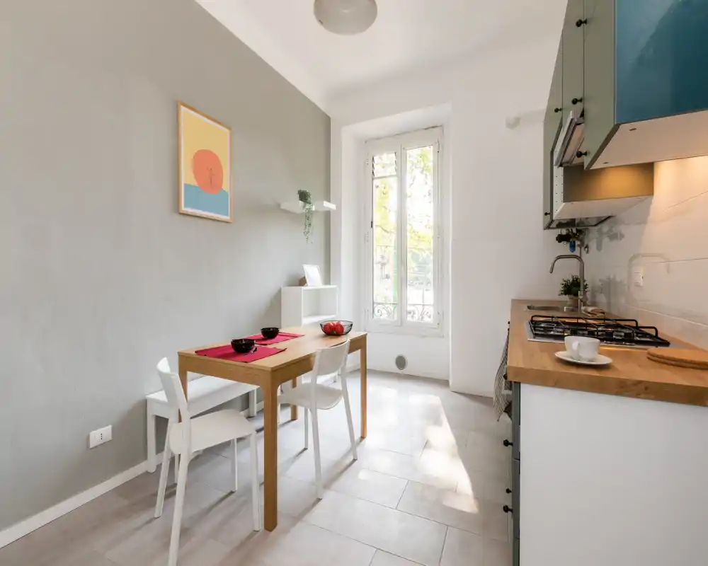 Cucina compatta e luminosa con piano in legno, piano cottura a gas e un piccolo tavolo da pranzo vicino a una finestra alta — spazio moderno e ben illuminato ideale per affitti in città.