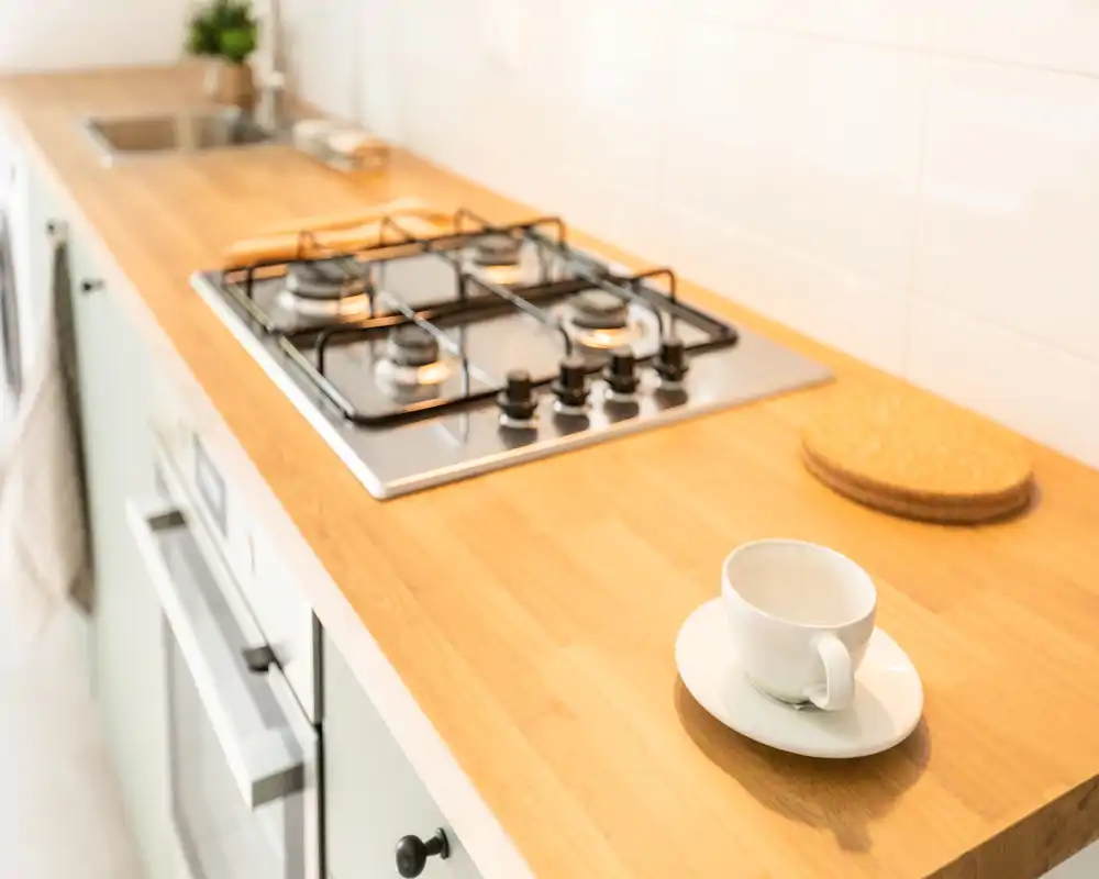 Piano di lavoro cucina luminoso e moderno con piano cottura a gas integrato, calda superficie in legno e una tazzina su piattino — perfetto per foto di annunci accattivanti.