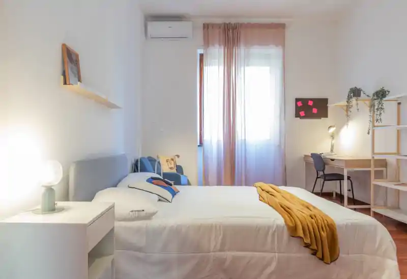 Bright, well-styled bedroom with a centrally placed double bed, cozy textiles and a small desk by the window — ideal for short-term rentals.