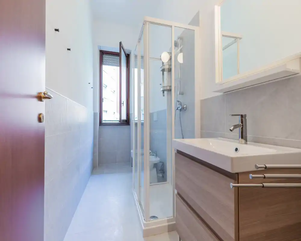 Modern, bright bathroom with a corner shower cubicle, wall-mounted sink cabinet, and a window providing natural light.