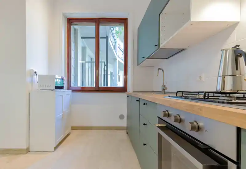 Cucina moderna e luminosa con piano in legno, forno incassato e piano cottura a gas, mobili ordinati e finestra che garantisce luce naturale.
