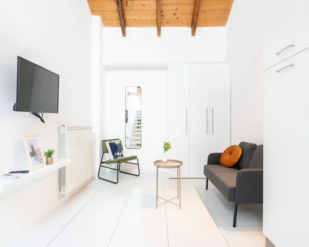 Soggiorno luminoso e minimal con divano compatto, poltrona e tavolino sotto un elegante soffitto in legno — perfetto per un annuncio moderno.