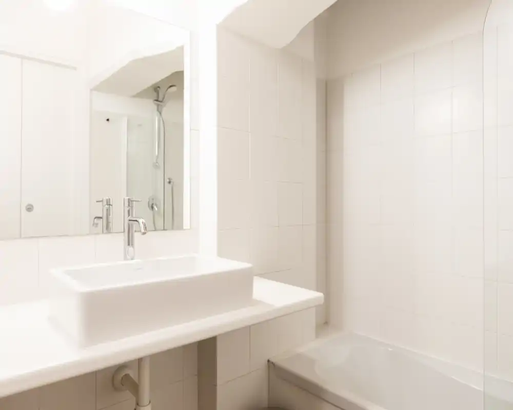 Bagno luminoso e minimalista con lavabo rettangolare da appoggio, specchio a parete e vasca/doccia piastrellata. Linee pulite e piastrelle neutre donano un aspetto moderno e fresco.