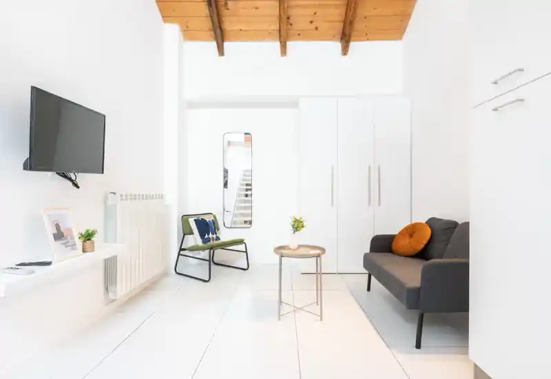 Sala de estar luminosa y minimalista con sofá compacto, butaca y mesita bajo un atractivo techo de madera — ideal para un anuncio moderno.