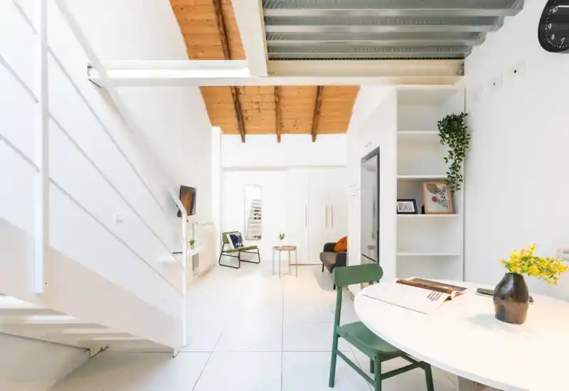 Espacio de estar moderno y luminoso con techo de madera tipo loft, paredes blancas, área de estar compacta y mesa pequeña — aireado y bien iluminado para anuncios.