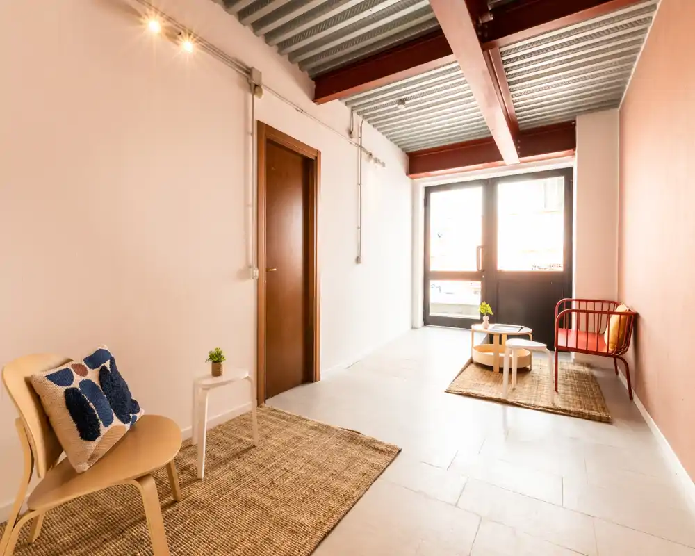 Zona giorno luminosa e minimal con luce naturale da una grande porta vetrata, tappeti intrecciati e sedute semplici—uno spazio moderno e tranquillo.