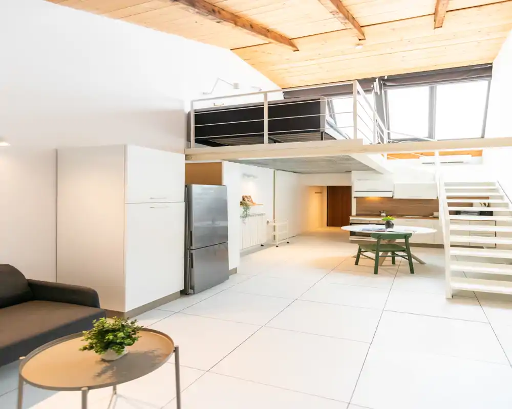 Amplia zona de estar tipo loft y luminosa con altillo, cocina moderna, sofá y mesa de comedor — diseño abierto perfecto para la vida en la ciudad.