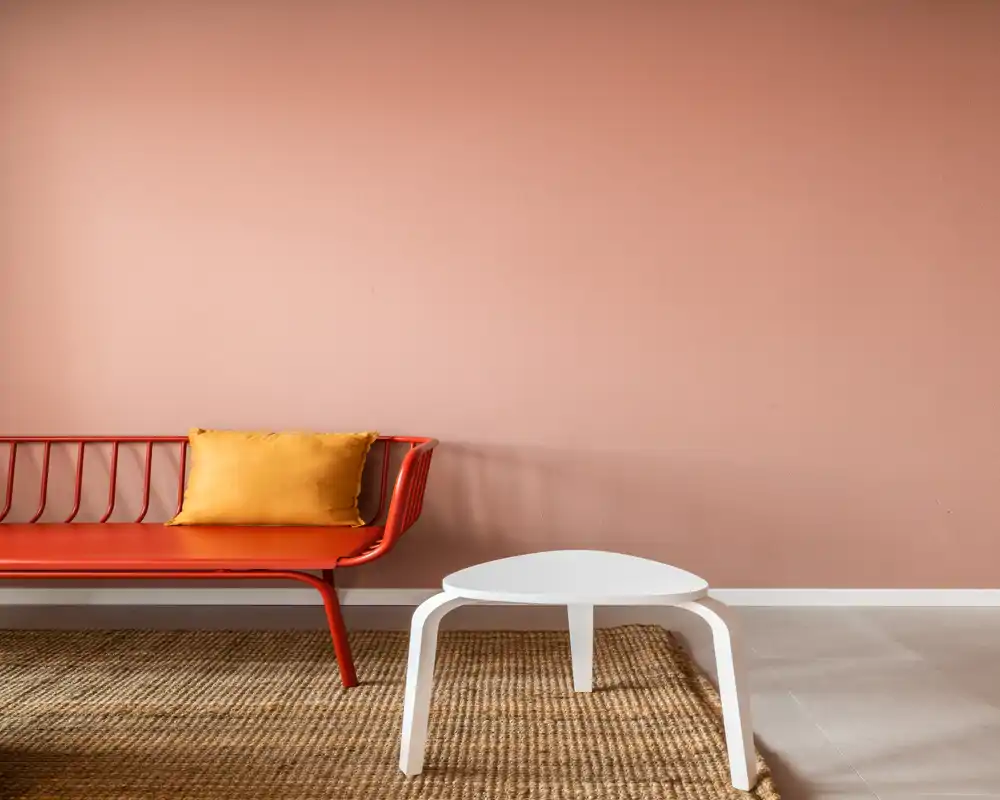 Zona de estar luminosa y moderna con un sofá rojo delgado, cojín mostaza y una mesa baja blanca sobre una alfombra de fibras — estilo cálido y minimalista ideal para alquileres.