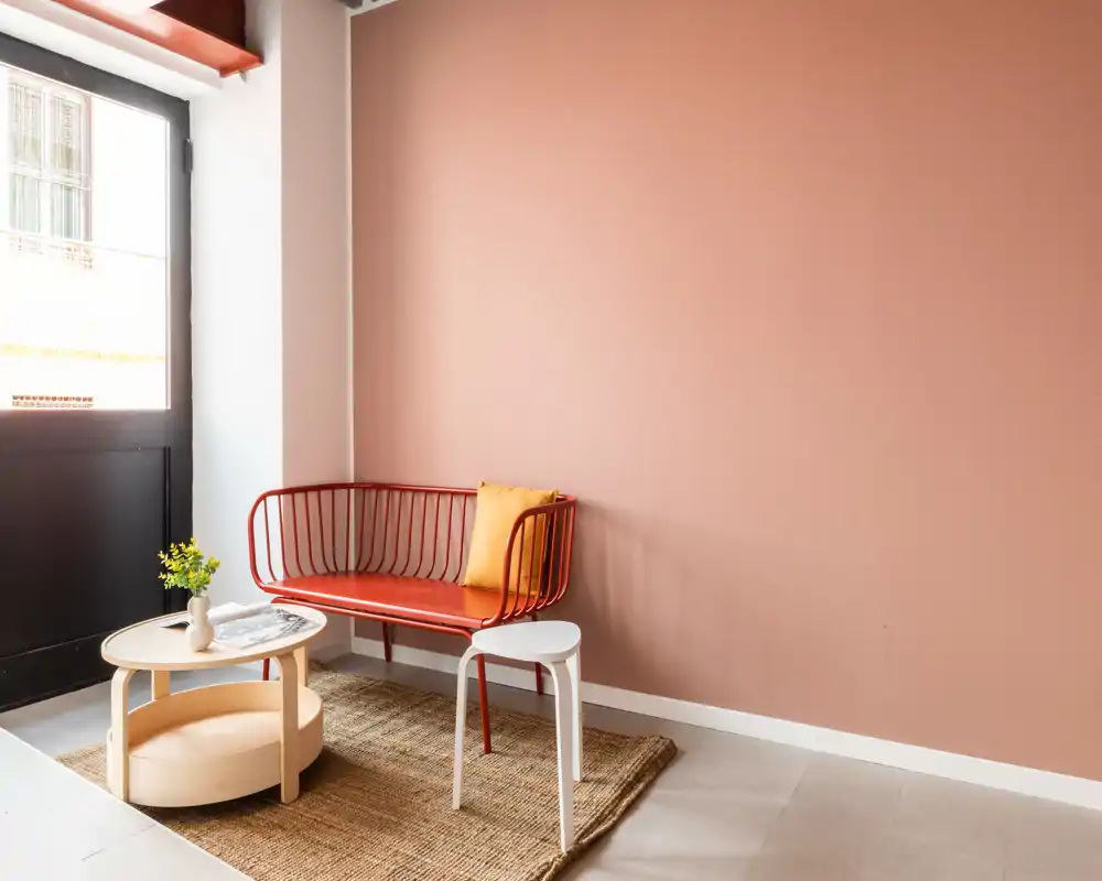 Zona de estar luminosa y con estilo con un banco metálico rojo, mesa de centro y alfombra de yute — ideal para un pequeño salón o recibidor.