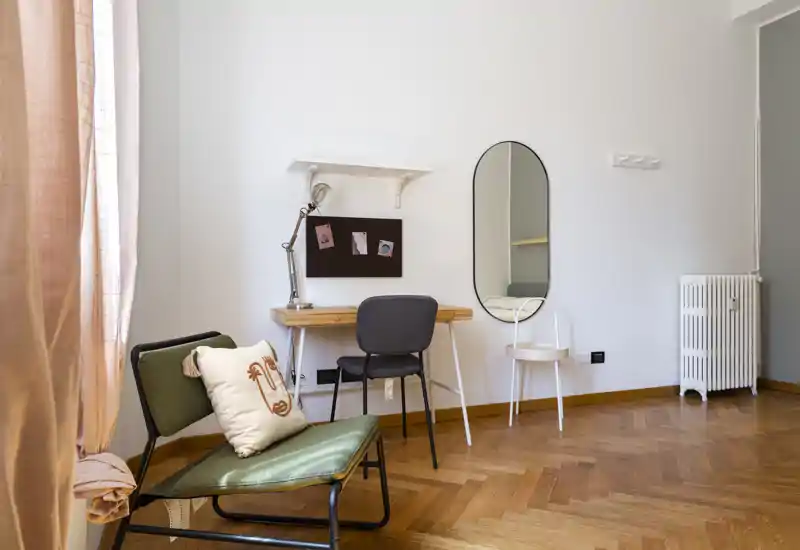 Rincón de la sala luminoso y estiloso con butaca, pequeño escritorio y espejo; suelo de parquet cálido y textiles suaves que crean un ambiente acogedor.