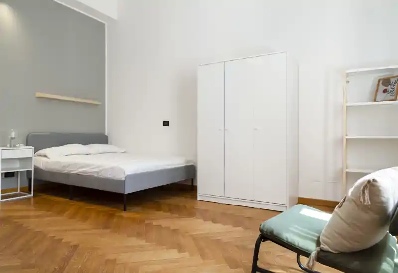 Dormitorio minimalista y luminoso con cama doble, armario blanco y suelo de parquet. Líneas limpias y luz natural crean un ambiente moderno y tranquilo, perfecto para anuncios.