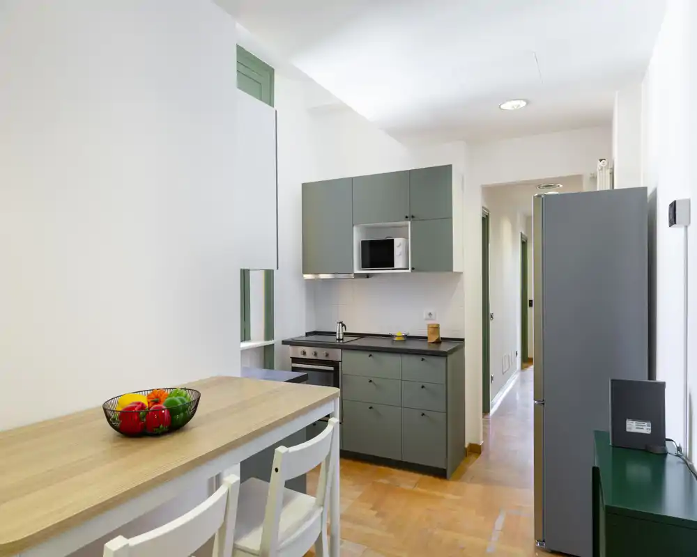 Cucina moderna compatta con mobili verde opaco, forno e microonde incassati e un bancone in legno con sgabelli — luminosa e ordinata, ideale per annunci.