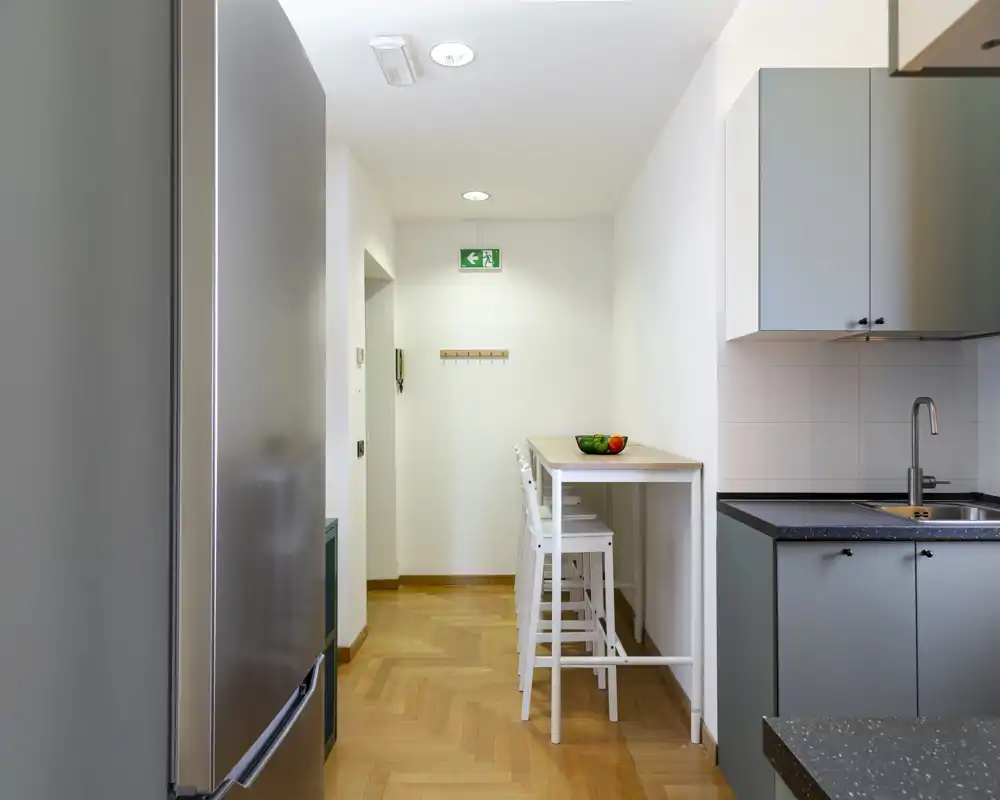 Cucina moderna compatta con frigorifero alto, lavello integrato e un bancone colazione con sgabelli — luminosa, ordinata e funzionale per un piccolo appartamento.