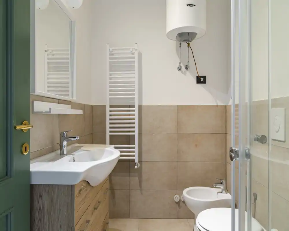 Bagno moderno e pulito con lavabo su mobile, bidet, pareti piastrellate, scaldasalviette e una doccia angolare visibile attraverso il vetro.