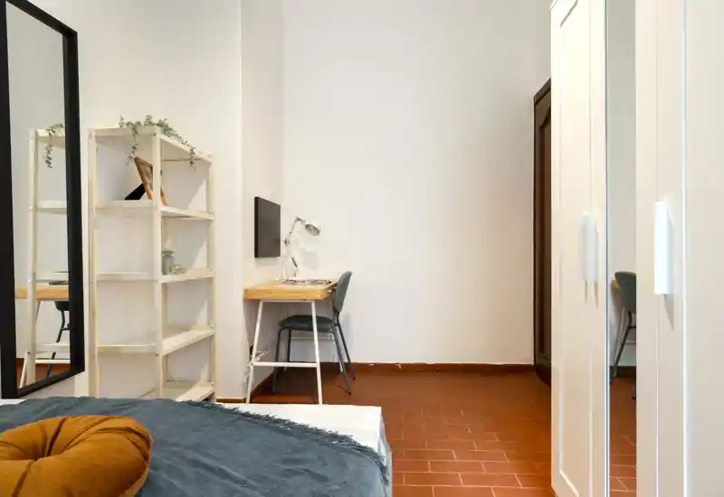 Dormitorio luminoso y sencillo con cama visible, escritorio pequeño y estantería — ideal para una o dos personas.