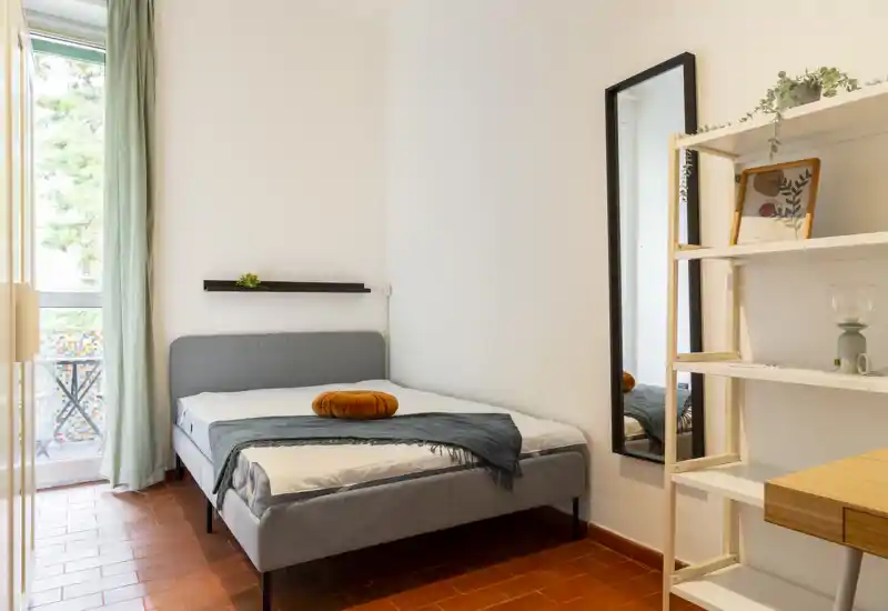 Dormitorio luminoso y ordenado con cama doble, textiles suaves y luz natural desde un pequeño balcón.