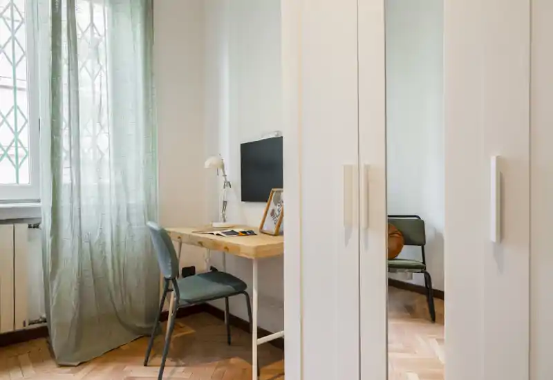 Rincón luminoso y arreglado con escritorio y silla junto a la ventana; textiles suaves y parquet cálido crean un ambiente acogedor.