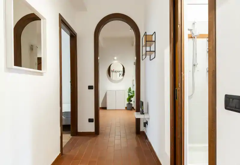 Bright, well-lit entrance corridor with terracotta floor tiles, arched doorway and clean white walls — a welcoming passage connecting rooms.