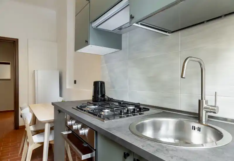 Modern compact kitchen with a stainless-steel sink, gas hob, oven and a small dining area. Clean lines and neutral tiles create a practical, well-lit cooking space ideal for short-term rentals.