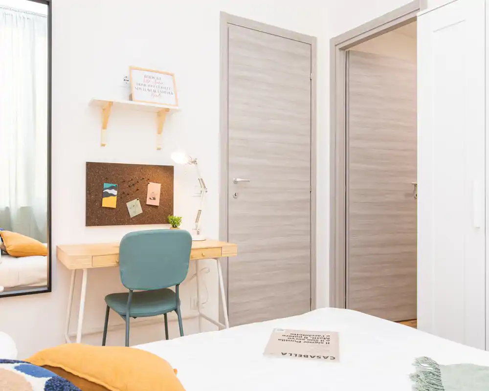 Camera da letto luminosa e ben sistemata con angolo letto visibile, una scrivania compatta e una sedia accogliente — ideale per una persona o per soggiorni brevi.