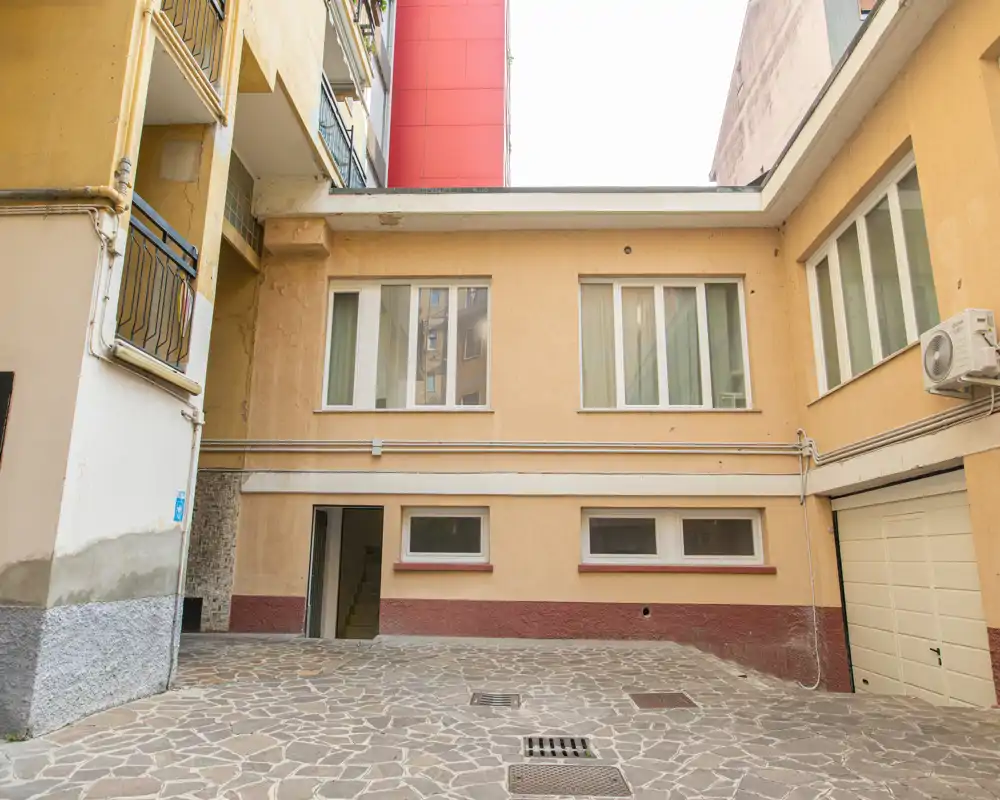 Piccolo cortile privato con pavimentazione in pietra, facciate, finestre e porta del garage — adatto per descrivere uno spazio esterno o area comune.