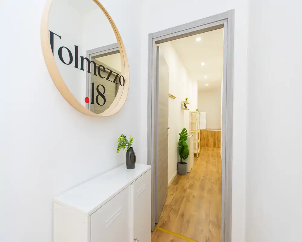 Ingresso luminoso e moderno con pavimento in legno, specchio rotondo e mobile contenitore compatto—stile minimale e pulito ideale per l'entrata di un appartamento.