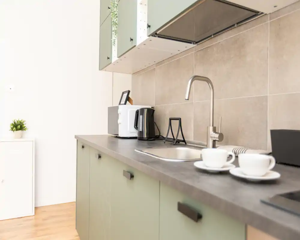 Cucinotto moderno e luminoso con lavello elegante, rubinetto e piccoli elettrodomestici; ante verde tenue e styling curato, perfetto per annunci.