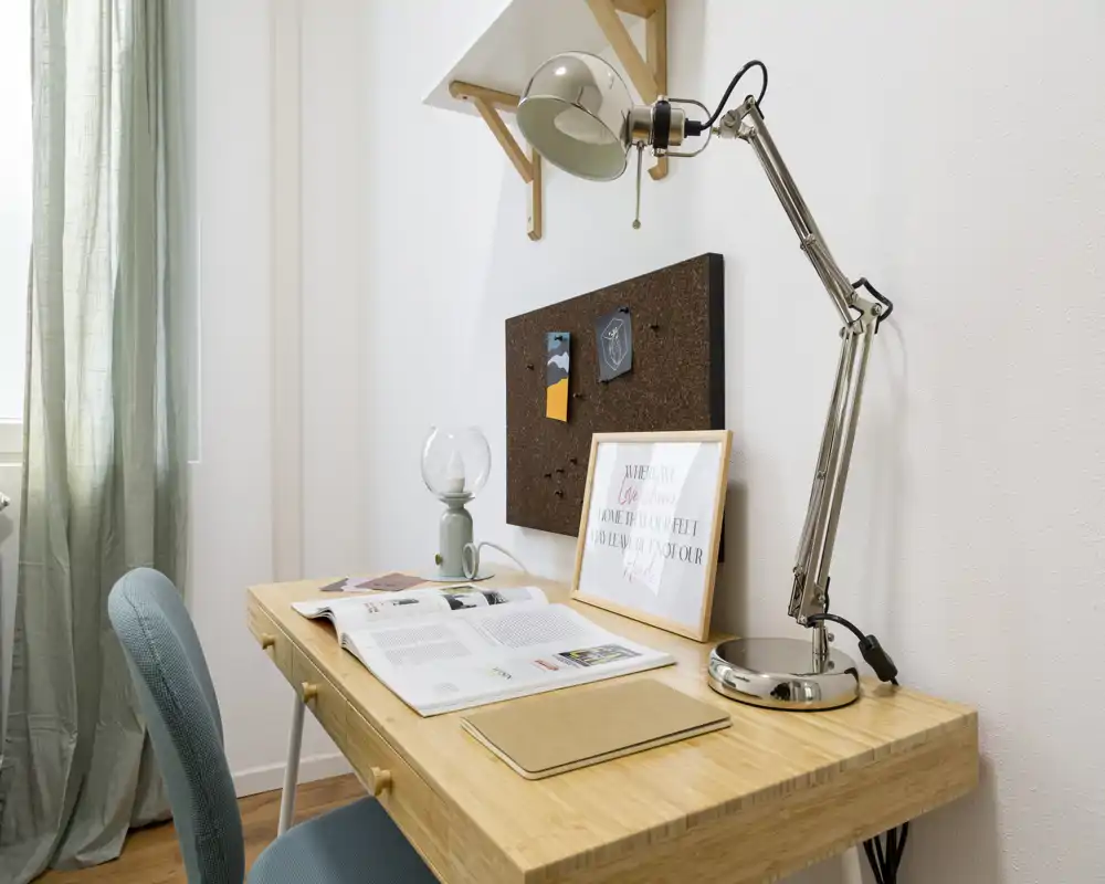 A compact, well-lit home workspace with a wooden desk, adjustable desk lamp and pinboard — ideal for studying or remote work.