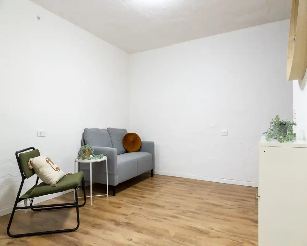 Piccolo soggiorno minimal ben arredato con divano due posti, poltrona, tavolino e piante — luminoso, ordinato e accogliente.