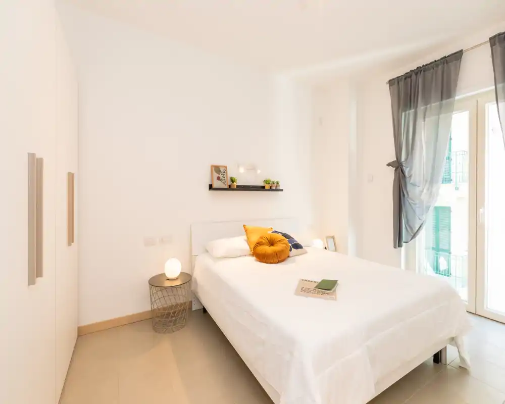 Bright, modern bedroom with a neatly made double bed, decorative cushions and natural light from a large window — ideal for rental listings.