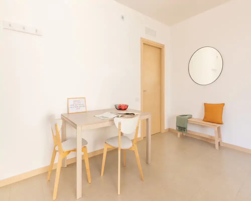 Minimal, bright dining corner with a small wooden table, two chairs and a bench with cushion; clean, Scandinavian-style decor ideal for a compact apartment.