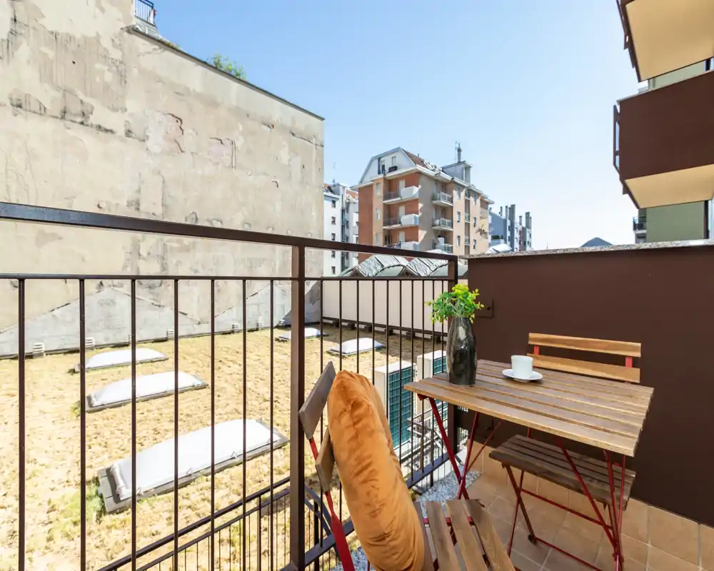 Sunny small balcony with a wooden bistro table and two folding chairs, a decorative vase and a coffee cup — ideal for morning coffee in the city.