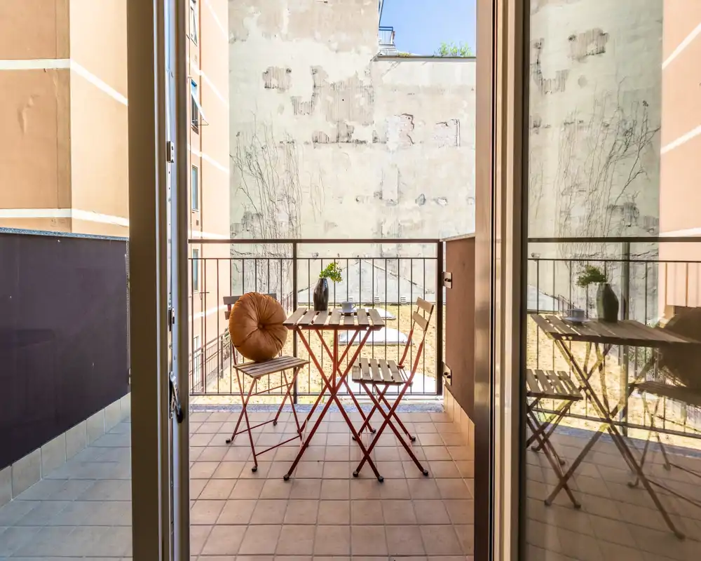 Sunny small balcony with a bistro table and two folding chairs, tiled floor and railing—ideal for morning coffee.