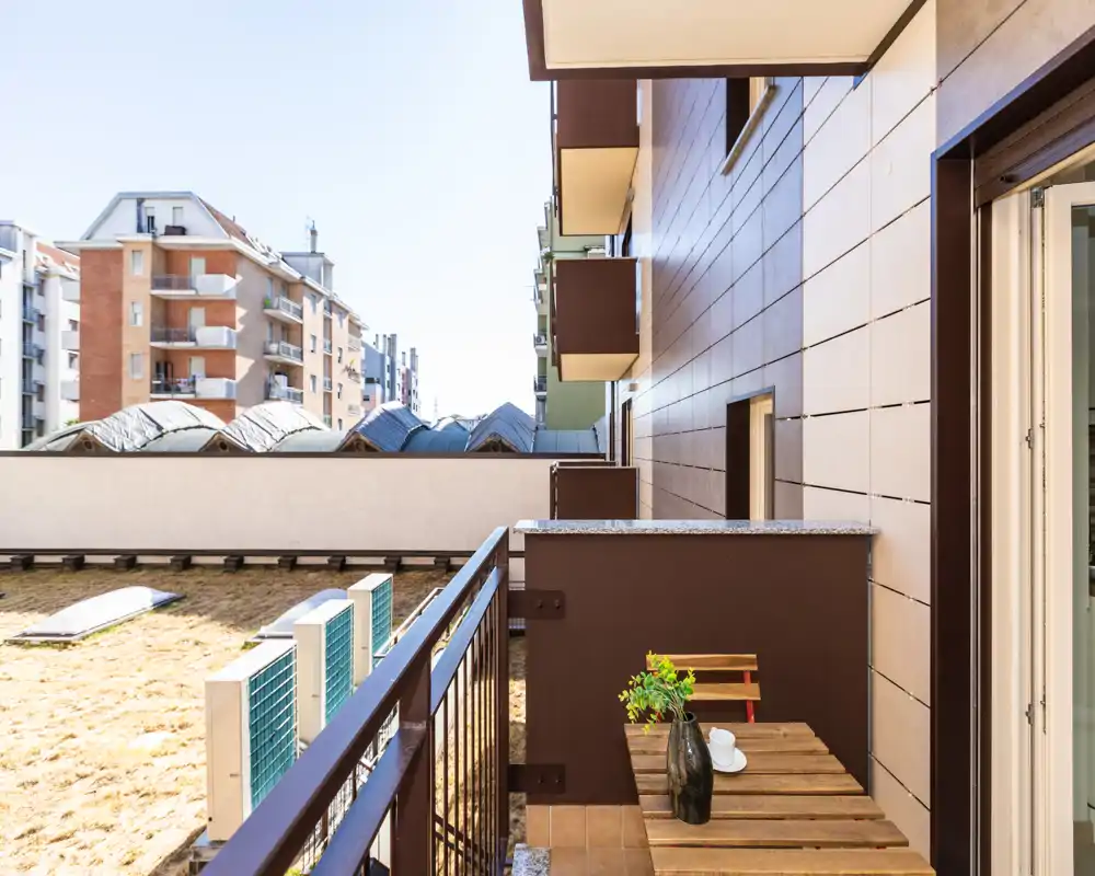 Sunny private balcony with a small wooden table and two chairs, overlooking neighboring buildings — bright and ideal for morning coffee.