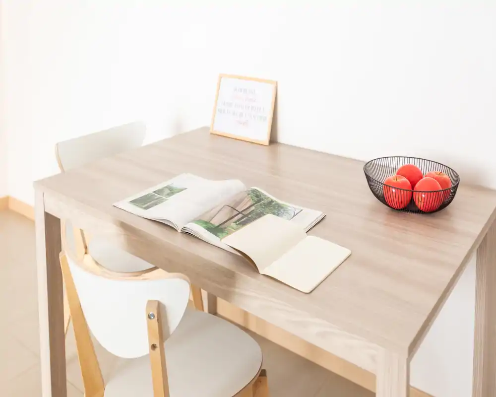 Minimalist dining nook with a light wooden table, two chairs, an open magazine and a fruit bowl — bright and uncluttered space ideal for relaxed breakfasts.