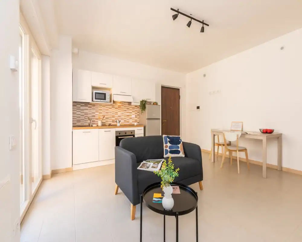 Bright, modern open-plan living area with a compact sofa, coffee table and a fitted kitchenette—perfect for a studio or small apartment.