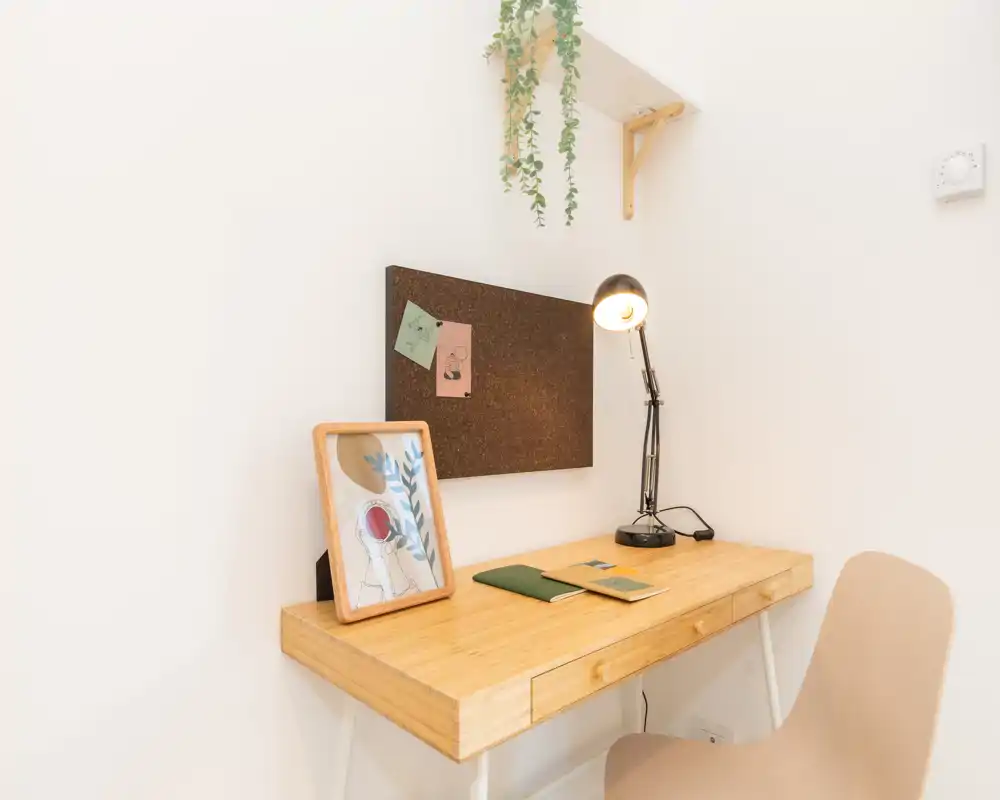Bright, minimalist workspace in a corner with a wooden desk, task lamp, corkboard and small decor — ideal for remote work or study.