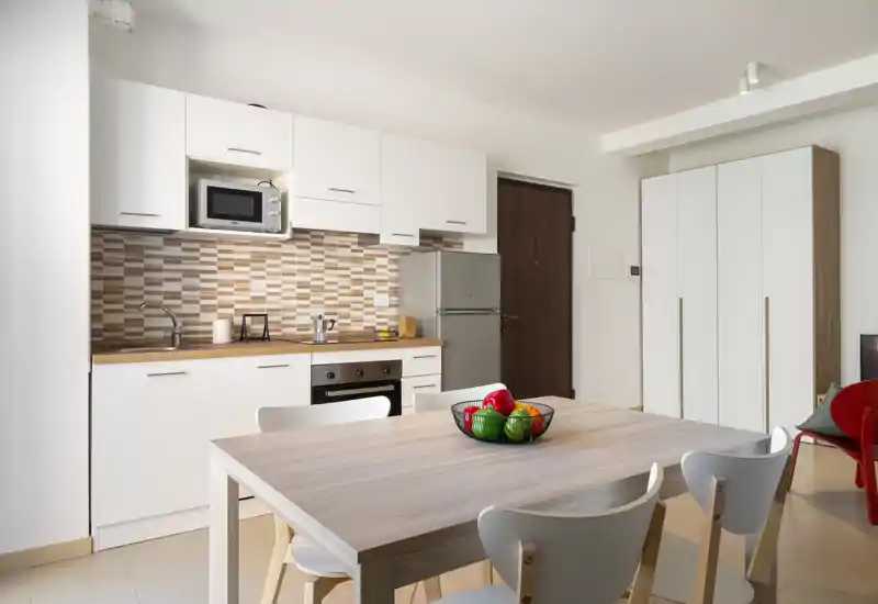 Bright, modern kitchenette with built-in appliances, wooden countertop and a dining table with chairs — ideal for a compact apartment.