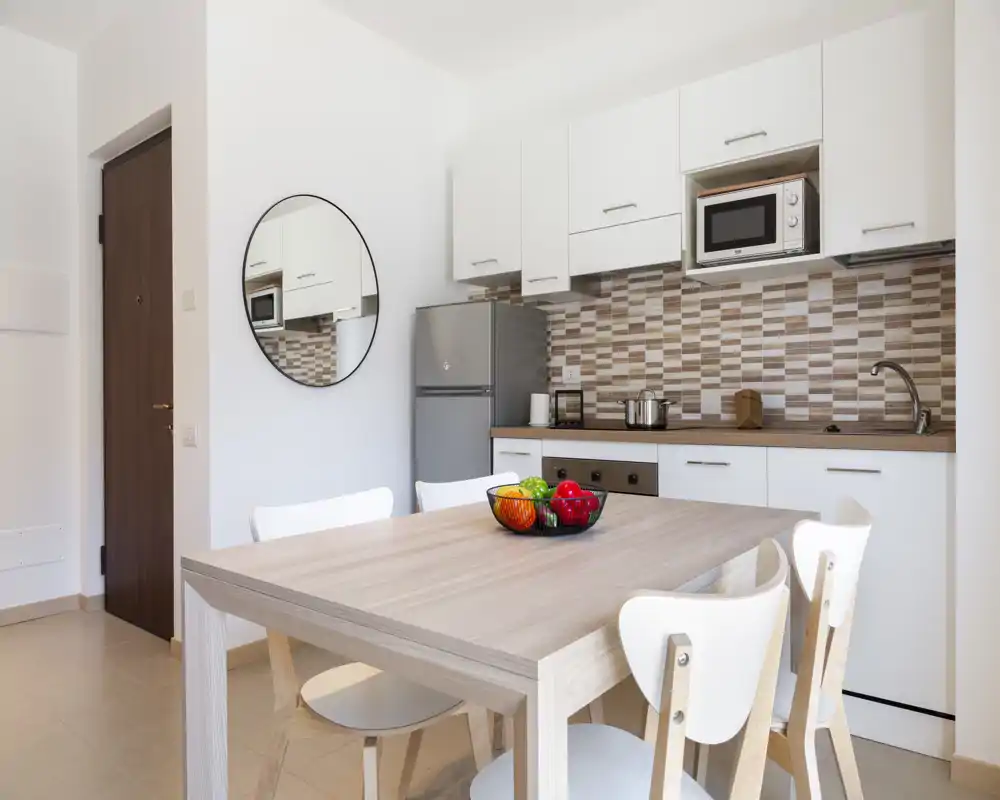 Bright, modern kitchenette with white cabinets, tiled backsplash and a dining table for four. Clean styling and natural light make it ideal for rental photos.