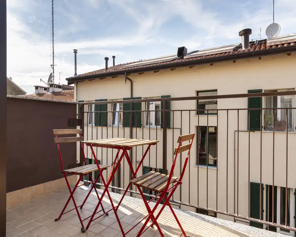 Pequeño balcón soleado con mesa plegable de madera y dos sillas a juego, suelo de azulejos y barandilla metálica — ideal para un café por la mañana o una pausa al aire libre.