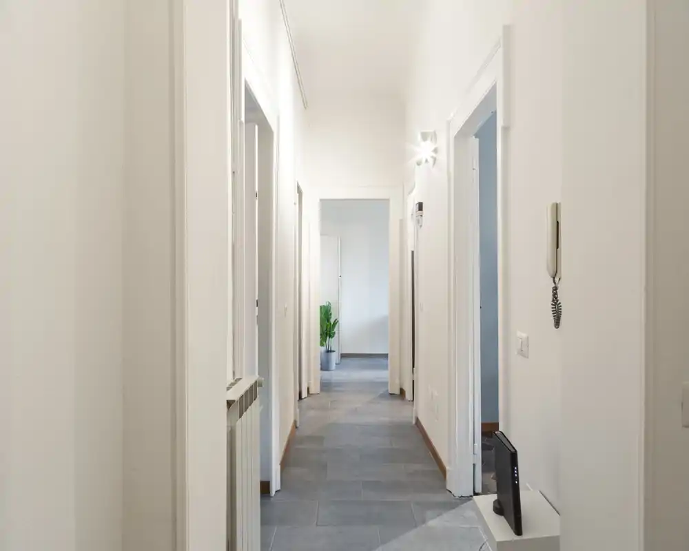 Entrada/pasillo luminoso y limpio con suelo de baldosas, paredes blancas y varias puertas; espacio ordenado y bien iluminado ideal para recibir invitados.