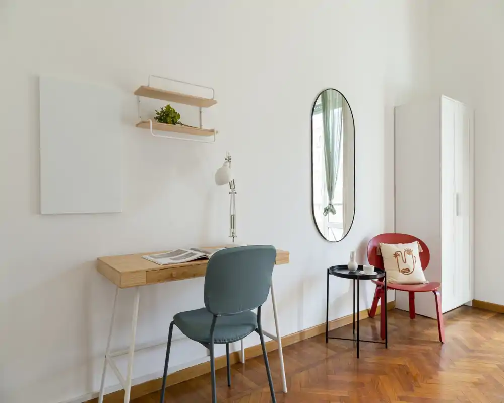 Rincón de sala luminoso y con estilo con un escritorio compacto, sillas cómodas, una pequeña mesa auxiliar y un espejo decorativo: ideal para relajarse o trabajar en un ambiente minimalista y acogedor.
