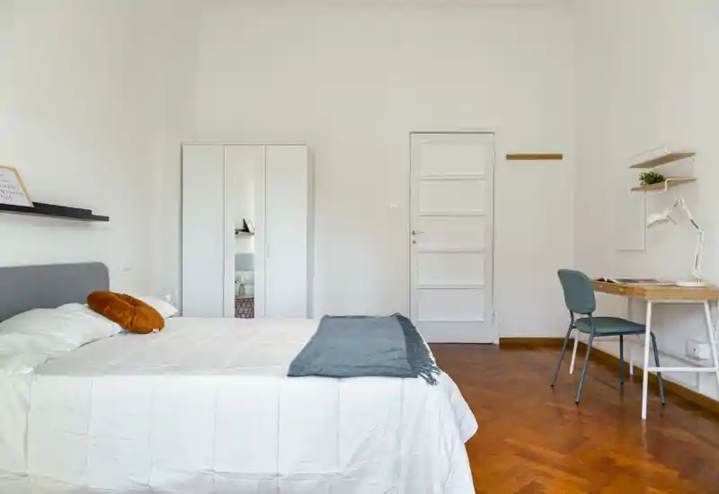 Dormitorio luminoso y minimalista con cama doble bien hecha, armario con espejo y escritorio compacto: ideal para alquileres de corta estancia que buscan confort limpio y funcional.