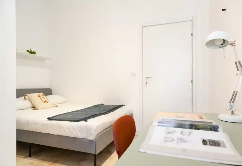 Bright, minimal bedroom with a double bed, soft linens and a small desk area. The room feels clean and well-lit with simple, contemporary decor.