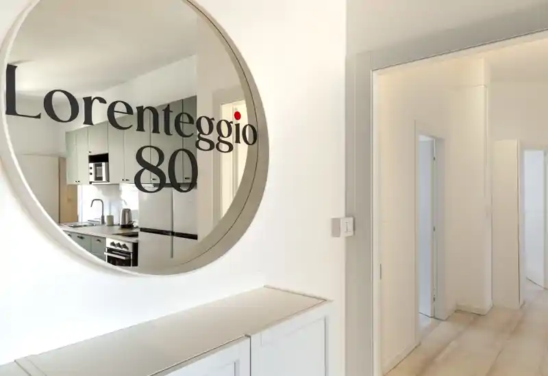 Entrada luminosa y moderna con espejo redondo que refleja la cocina contigua: líneas limpias, tonos neutros y un pequeño mueble ideal para llaves y correo.